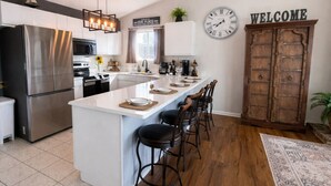 A modern kitchen with a central island, bar stools, a stainless steel refrigerator, and a wooden cabinet. - Stillwater Shores Lakefront 2bd/2BA Pool, Hot Tub 6PP (Village of Four Seasons)