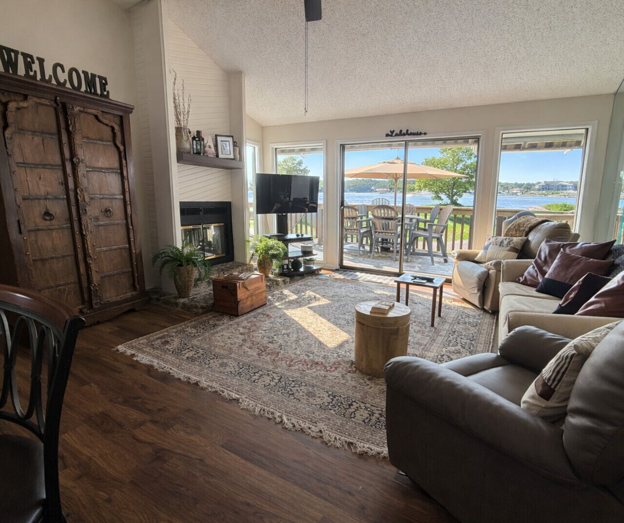 Una sala de estar con piso de madera, un tapete grande, un sofá, un televisor y vistas al exterior a través de amplias ventanas.