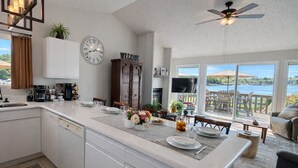 A modern kitchen with a central island, white cabinetry, and a dining area with a view of the outdoors. - Stillwater Shores Lakefront 2bd/2BA Pool, Hot Tub 6PP (Village of Four Seasons)