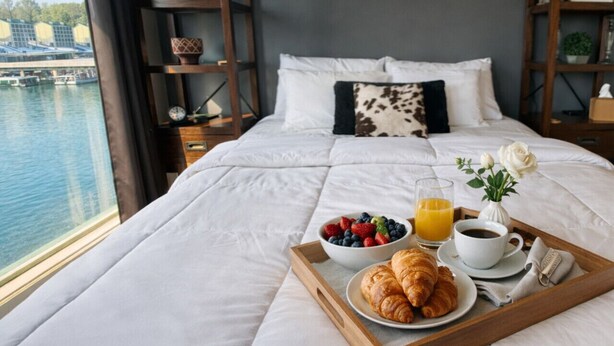 A hotel room with a large bed, a breakfast tray with croissants, fruit, and juice, and a view of a body of water. - Stillwater Shores Lakefront 2bd/2BA Pool, Hot Tub 6PP (Village of Four Seasons)