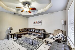 A living room with a sectional sofa, a coffee table, a floor lamp, a ceiling fan, and a window with blinds. - Hot Tub! Dog-friendly Gem 6 Mi to Dtwn Brownsville (Brownsville)