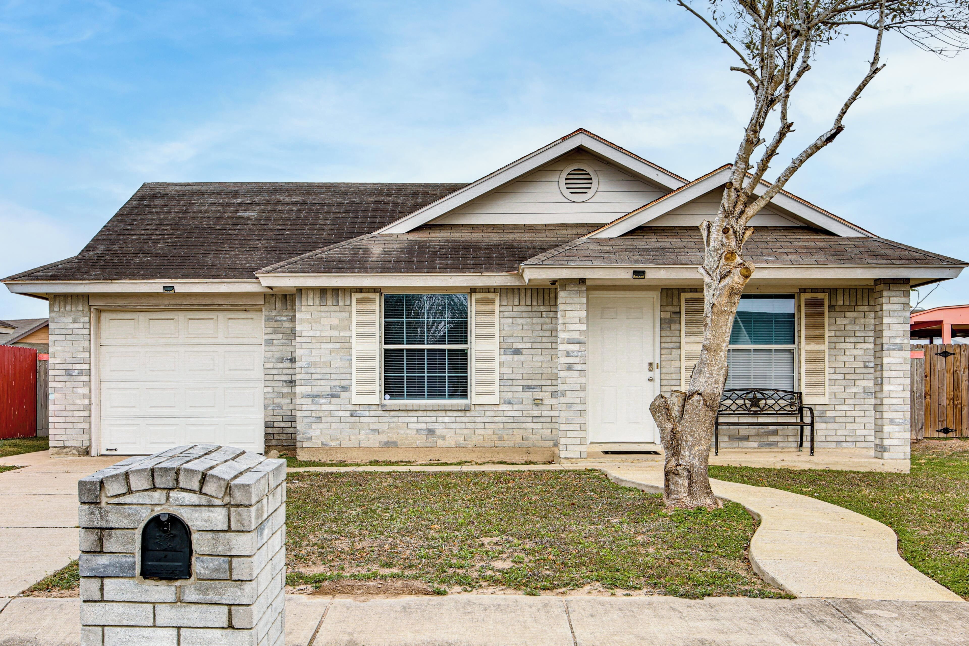 A single-story house with a garage, a small front yard, and a tree.