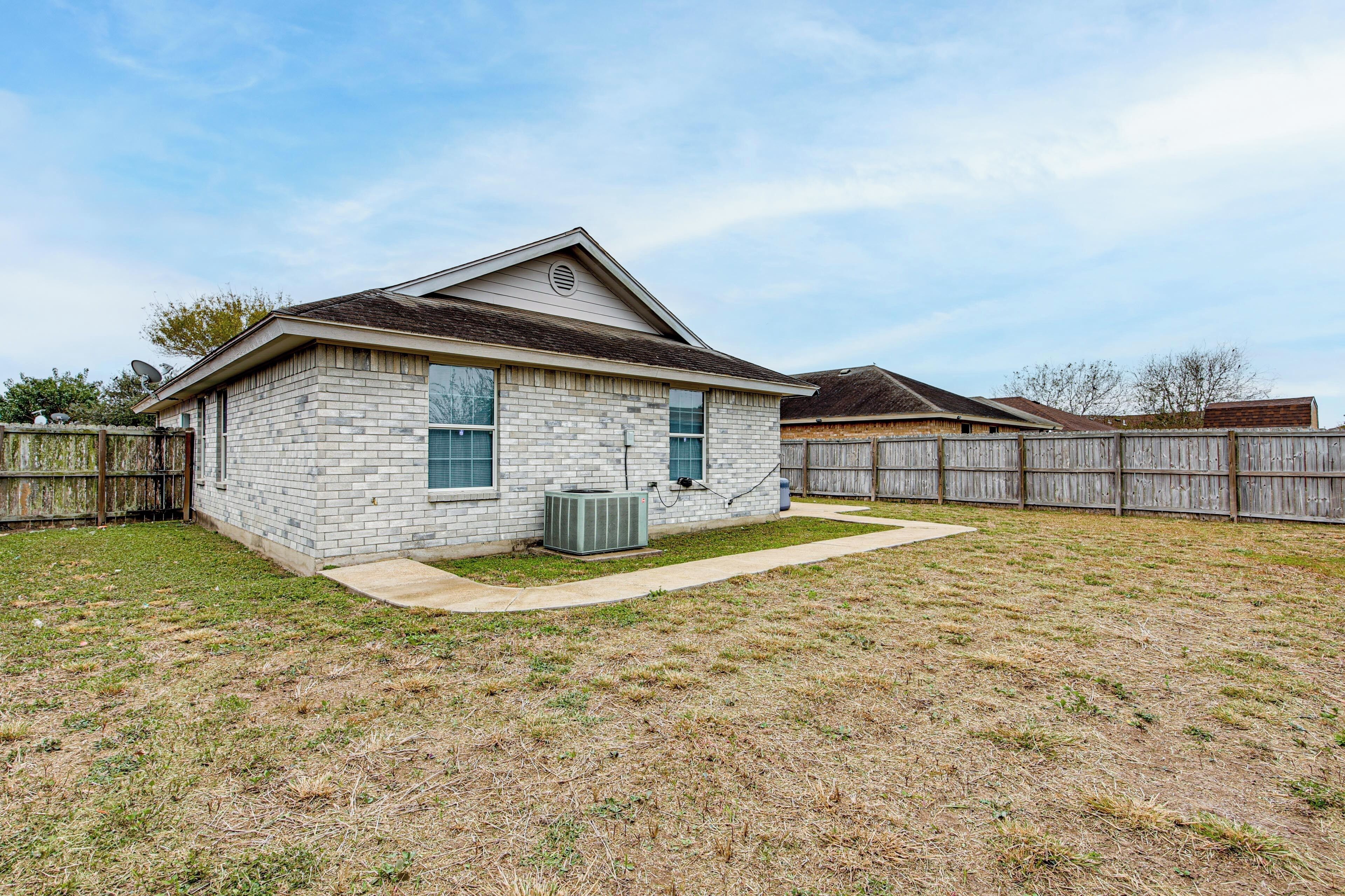 A single-story house with a brick exterior, a small front yard, and a wooden fence.