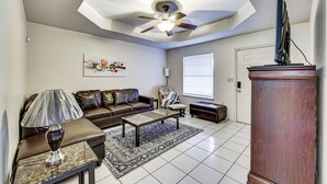 A living room with a ceiling fan, a sofa, a coffee table, a lamp, a TV on a stand, and a window with blinds. - Hot Tub! Dog-friendly Gem 6 Mi to Dtwn Brownsville (Brownsville)