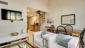 A modern living room with a white sofa set, a glass coffee table, a flat-screen TV mounted on the wall, a wooden dining table with chairs, and a spiral staircase leading to an upper level. - Golf, Swim & Dine! Condo w/ Lake Conroe Access (Montgomery)