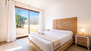Ein Schlafzimmer mit einem großen Bett, einem hölzernen Kopfteil, zwei Nachttischen mit Lampen, einer Schiebetür zu einer Terrasse und einem Holzboden.