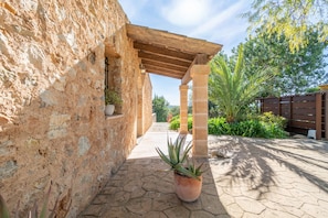 Un edificio in pietra con una pergola in legno, piante in vaso e un vialetto lastricato.