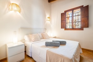 Una camera da letto con un letto, comodini, applique, una finestra con persiane e un lampadario.