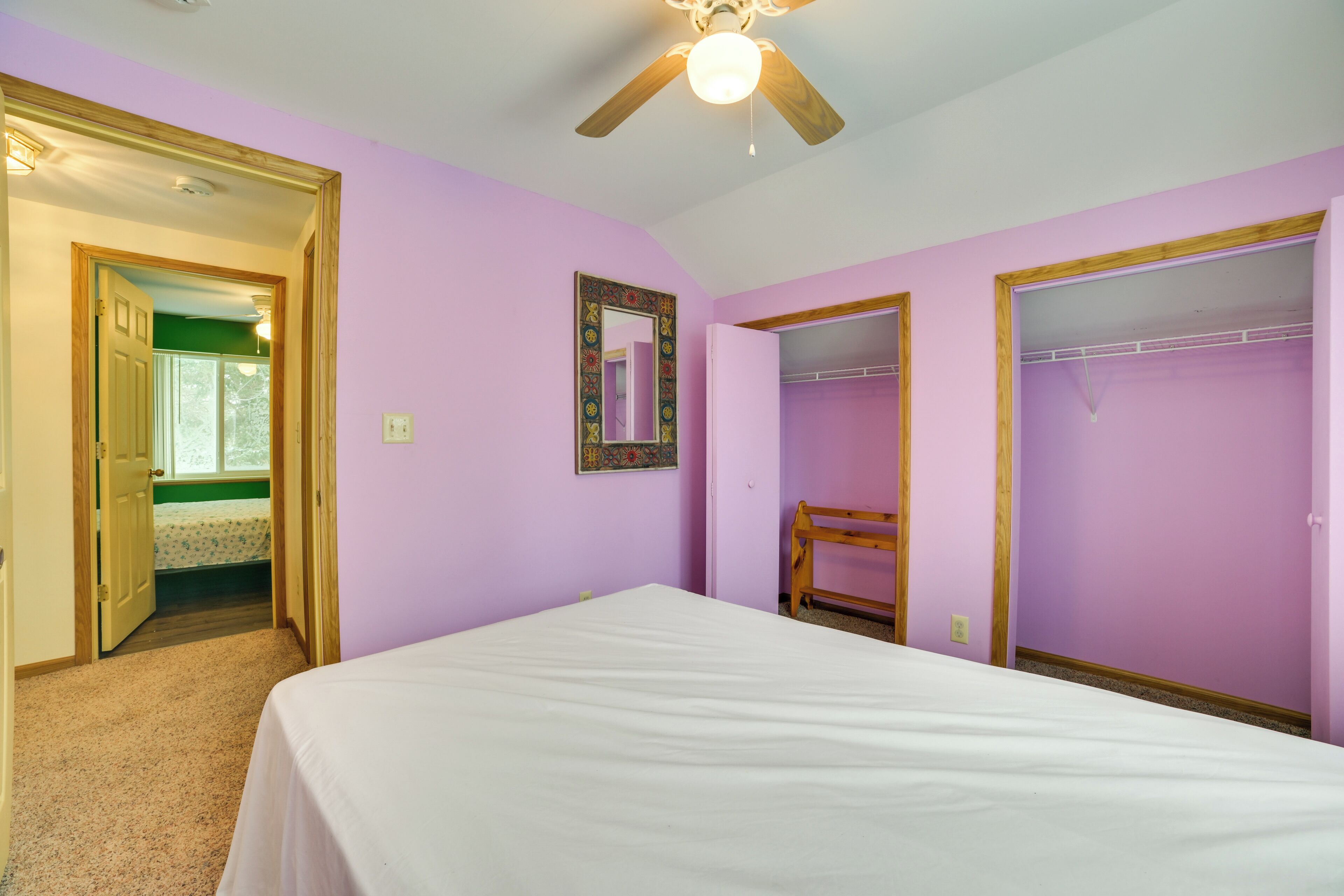 A bedroom with a bed, a ceiling fan, a walk-in closet, and a door leading to another room.