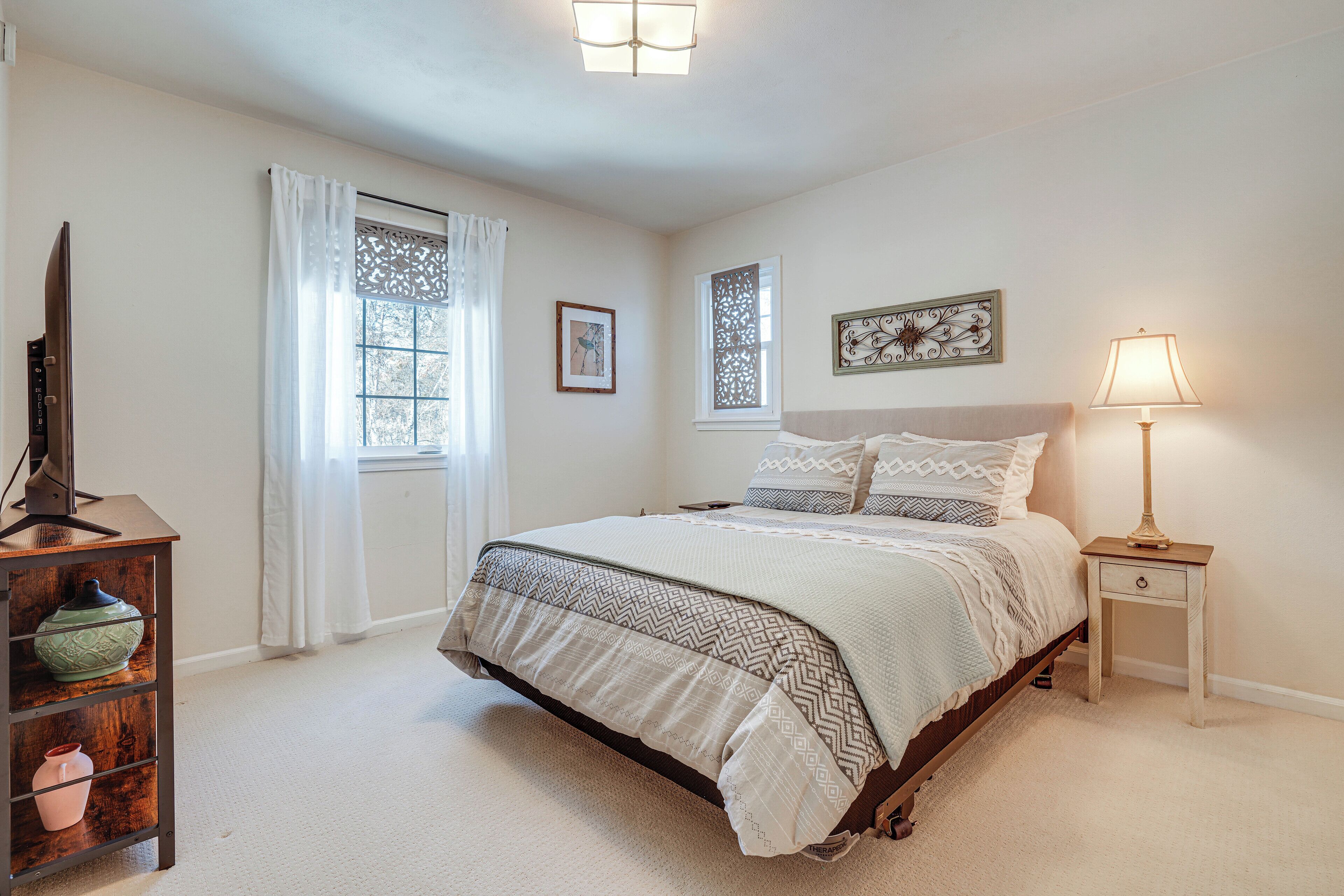 A bedroom with a bed, a nightstand, a lamp, a TV, and a shelf with decorative items.