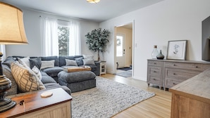Een moderne woonkamer met een grijze bank, een houten salontafel en een grote plant.