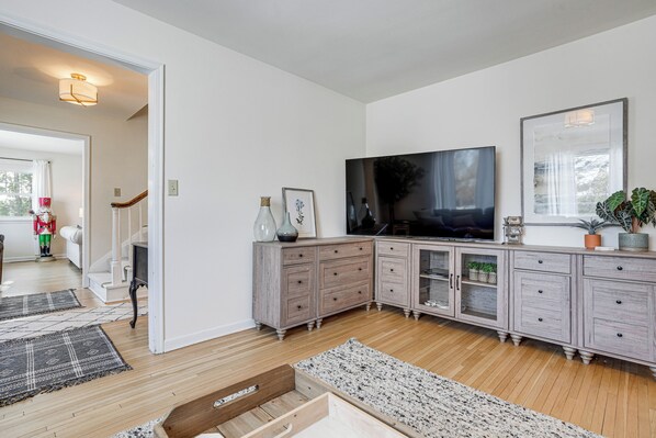 A spacious living room with a large flat-screen TV, wooden cabinets, and a staircase leading to another room. - Spacious Home Near Lake Bemidji With Game Room! (Bemidji)