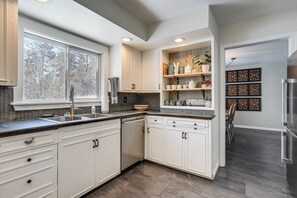 A modern kitchen with white cabinetry, a built-in dishwasher, and a large window providing a view of trees. - Spacious Home Near Lake Bemidji With Game Room! (Bemidji)