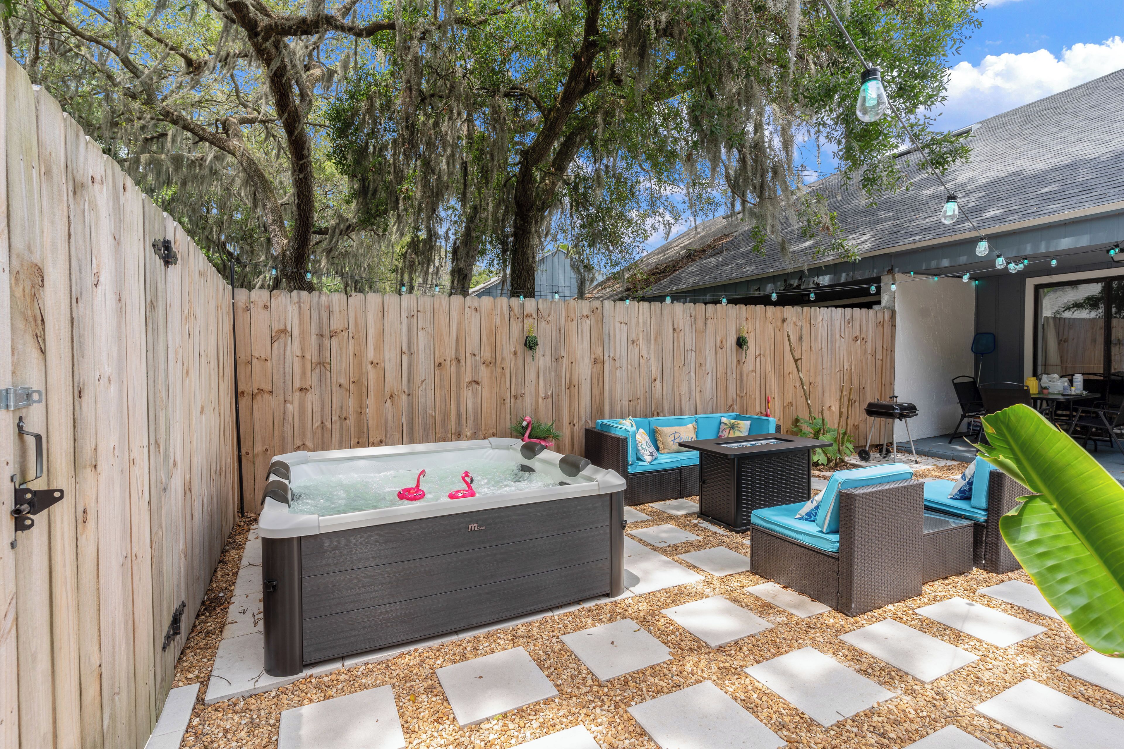 Un patio trasero con un jacuzzi, mobiliario exterior y una valla de madera.