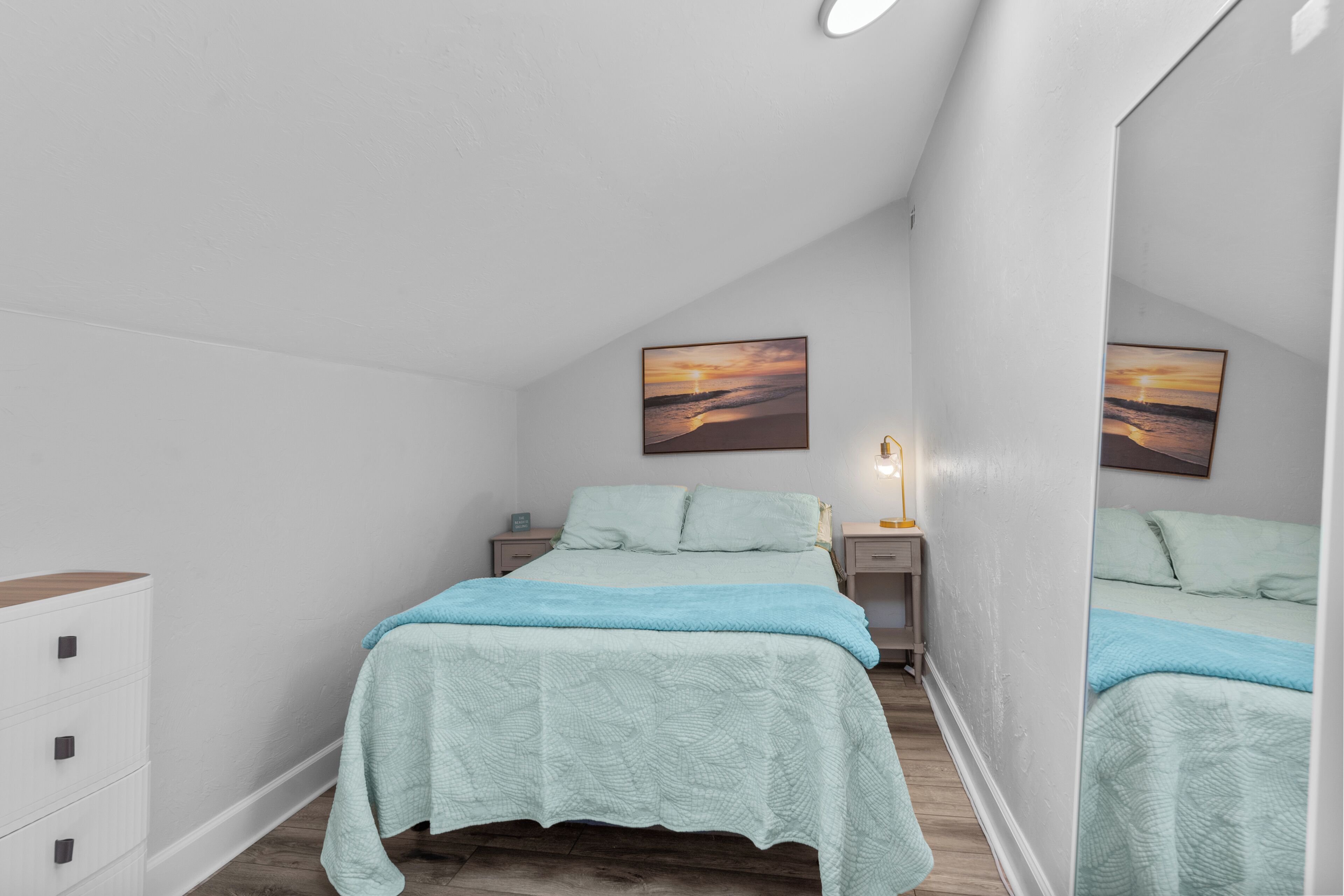 Un dormitorio con cama, mesitas de noche, cómoda y dos cuadros colgados en la pared.