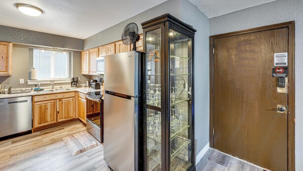 A modern kitchen with wooden cabinets, a stainless steel refrigerator, a glass-fronted pantry, and a wooden door with a 'No Smoking' sign. - Easily Explore Anchorage! Modern Duplex Near Town (Anchorage)