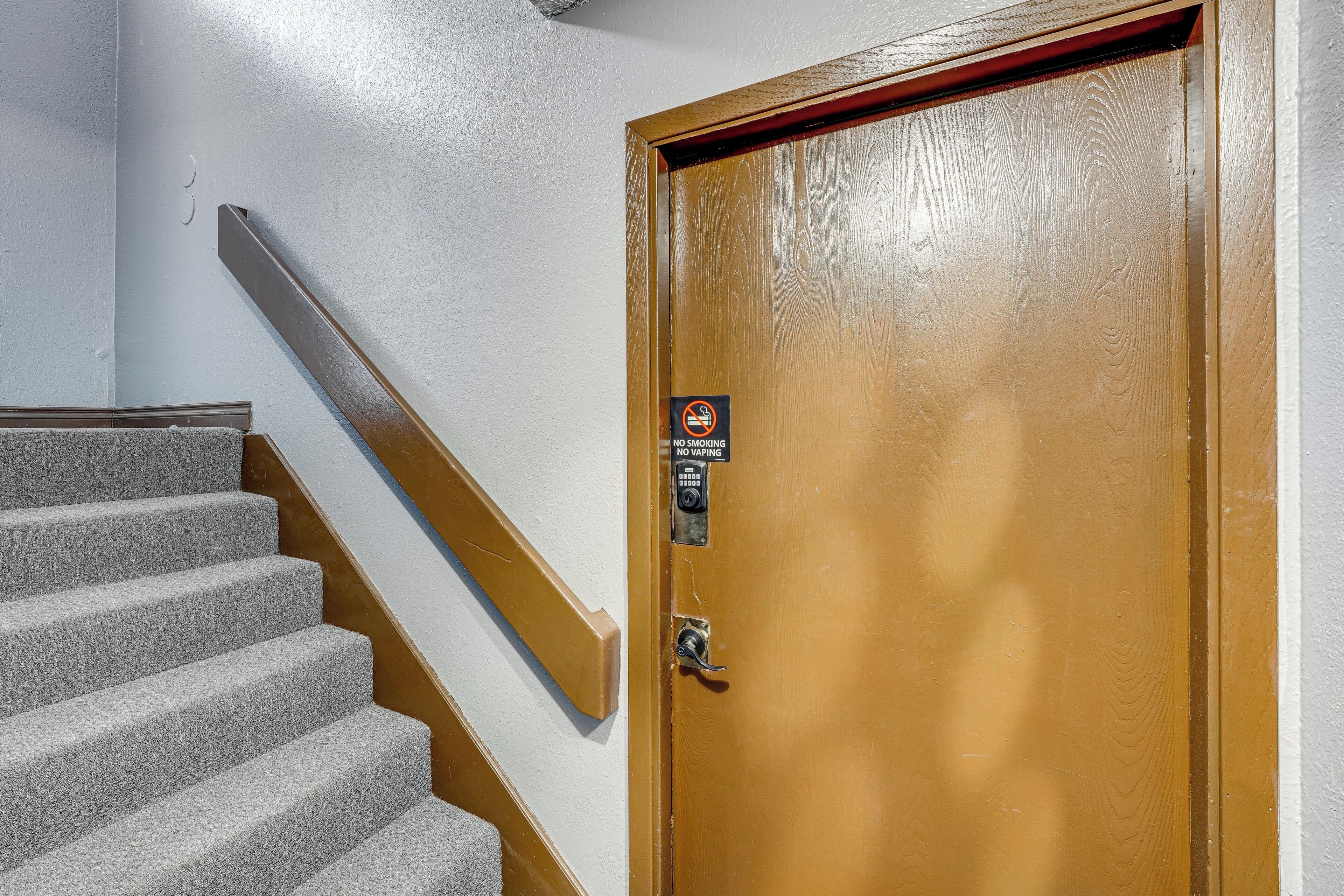 Una puerta de madera con un cartel de prohibido fumar, un teclado de cierre y una escalera con peldaños alfombrados.