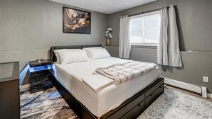 A bedroom with a bed, nightstand, and a painting on the wall. - Easily Explore Anchorage! Modern Duplex Near Town (Anchorage)