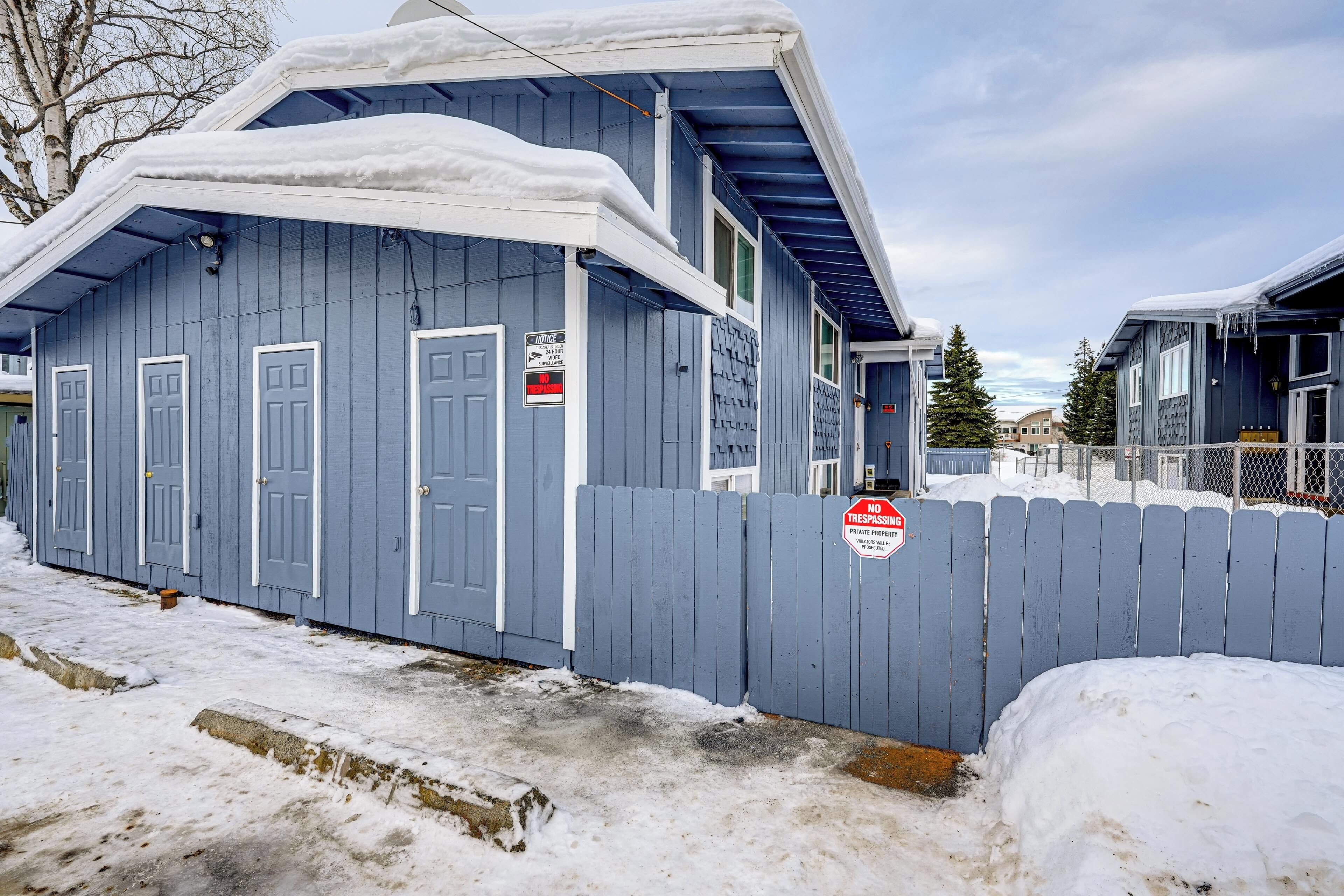 A blue building with multiple doors, a fenced area, and a 'No Trespassing' sign.