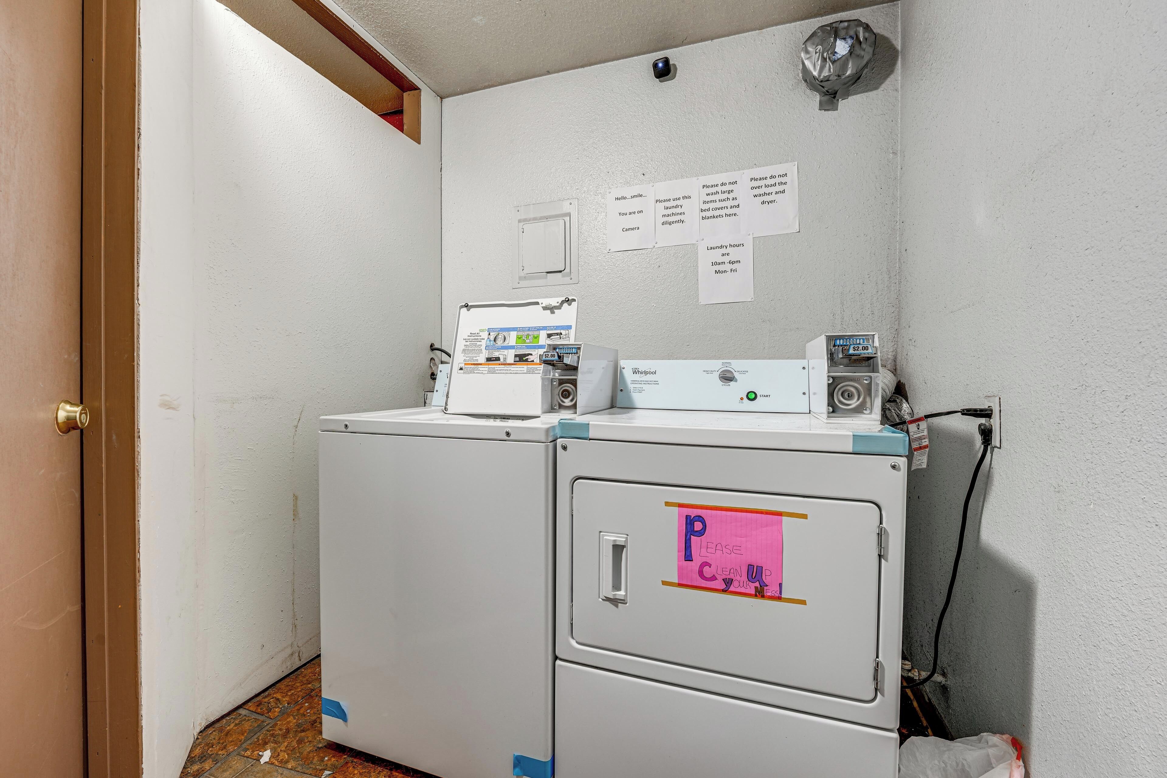 A laundry area with two washing machines, a dryer, and a wall-mounted security camera.