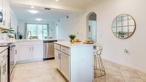 A modern kitchen with white cabinetry, a central island, and a round mirror on the wall. - Play & Stay: 1st Floor Ava Maria Condo! (Immokalee)