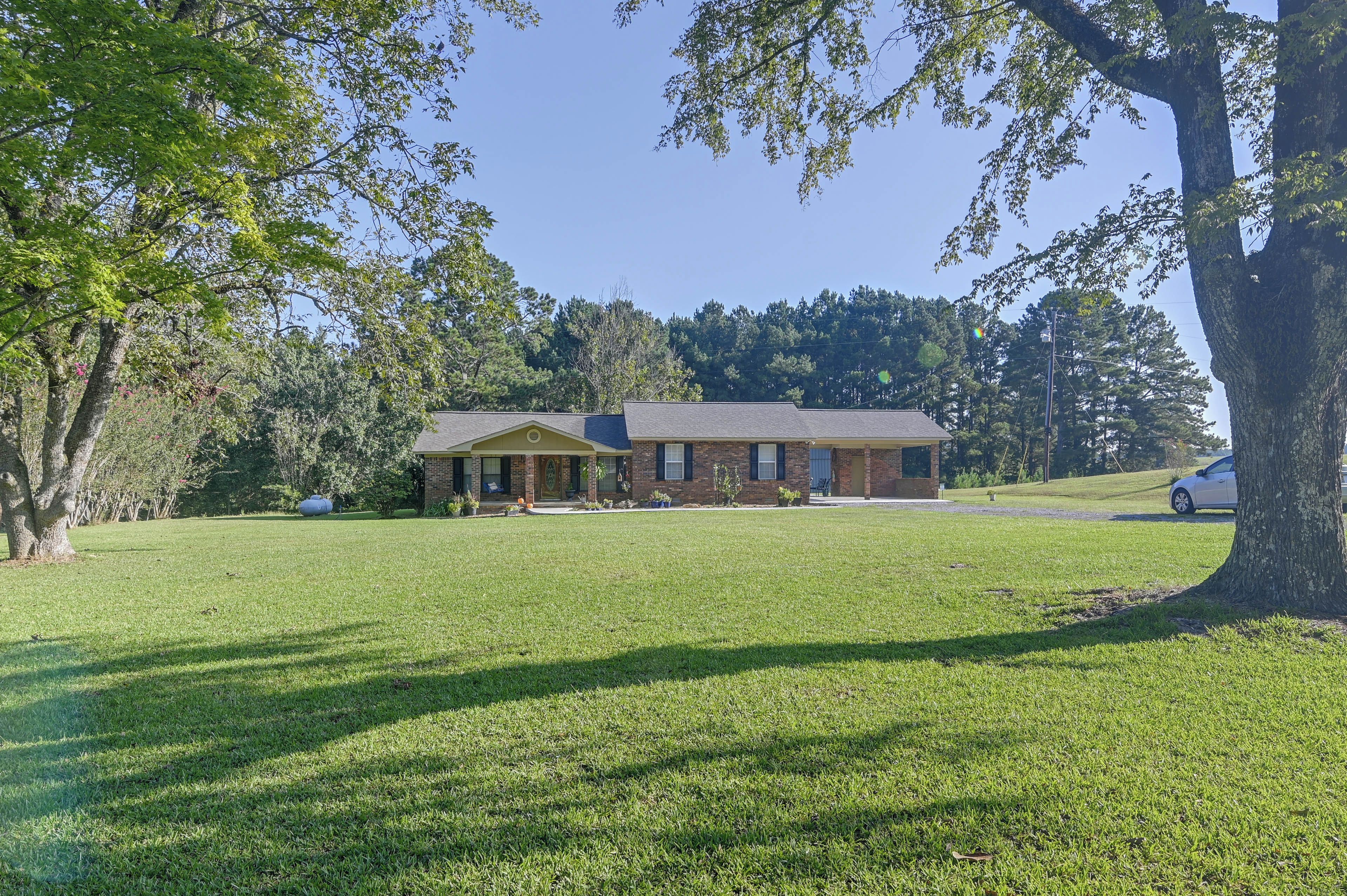 A single-story brick house with a covered porch, surrounded by a well-maintained lawn and trees.