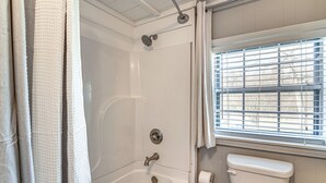 A bathroom with a bathtub, toilet, and window with blinds.