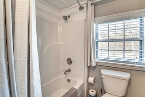 A bathroom with a bathtub, toilet, and window with blinds.