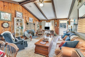 A cozy living room with a fireplace, wooden walls, a sofa, and a television. - Noxapater Fall Retreat for Hunting & MSU Games (Noxapater)