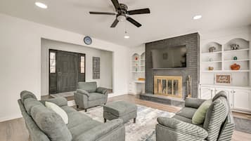 Un salon moderne avec des canapés gris, une cheminée, un ventilateur de plafond et un téléviseur fixé au-dessus de la cheminée.