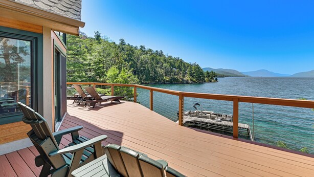 Eine Holzterrasse mit Stühlen und einem Tisch, mit Blick auf einen See mit Steg und Bäumen.