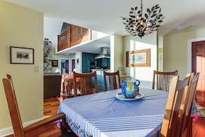 A dining area with a table set for four, wooden chairs, a chandelier, and a view of the kitchen and living room. - Year-round Fun in Putnam Station: Lakefront Home! (Town of Putnam)