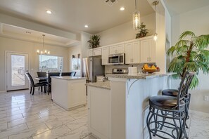 A modern kitchen with white cabinets, granite countertops, and stainless steel appliances. There are two bar stools and a dining area with a table and chairs. - Mountain-view Retreat Near Organ Wilderness Trails (Las Cruces)
