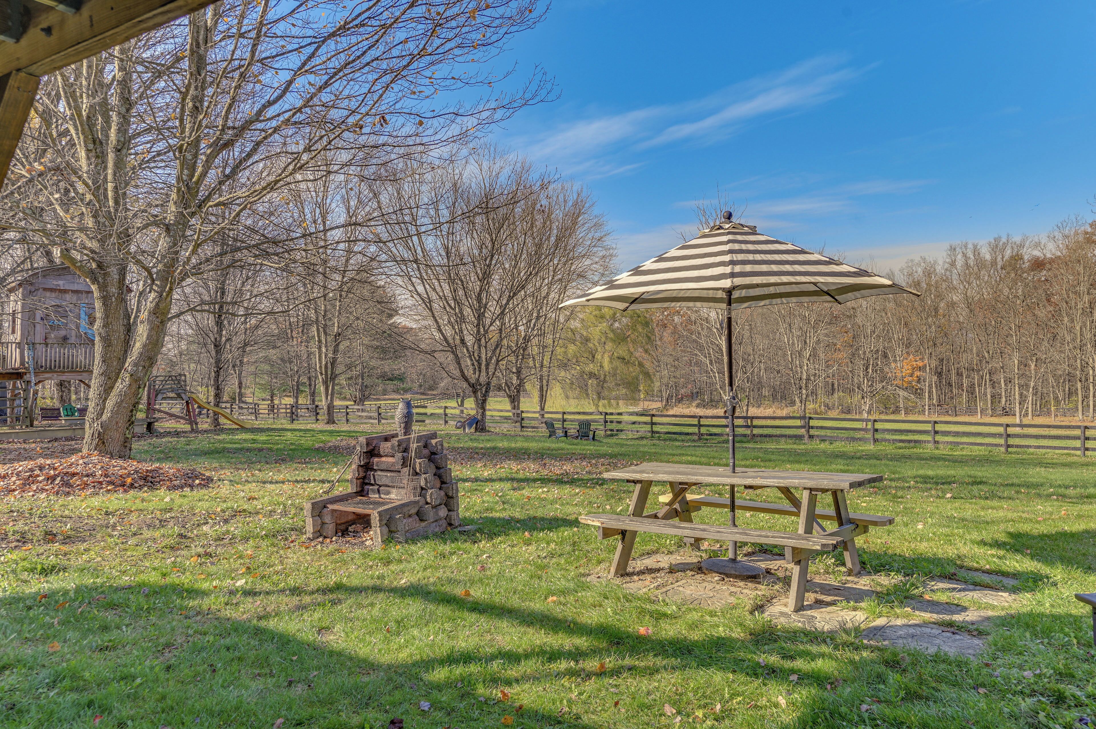 A picnic area with a wooden table and bench, a striped umbrella, and a stone fireplace.