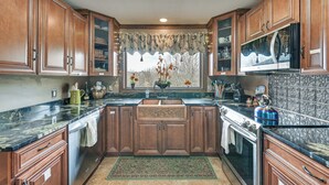 A kitchen with wooden cabinets, a granite countertop, a stainless steel sink, and a window with a view of trees. - Beautiful & Unique Farmhouse 15 Mi to Saratoga (Fort Edward)