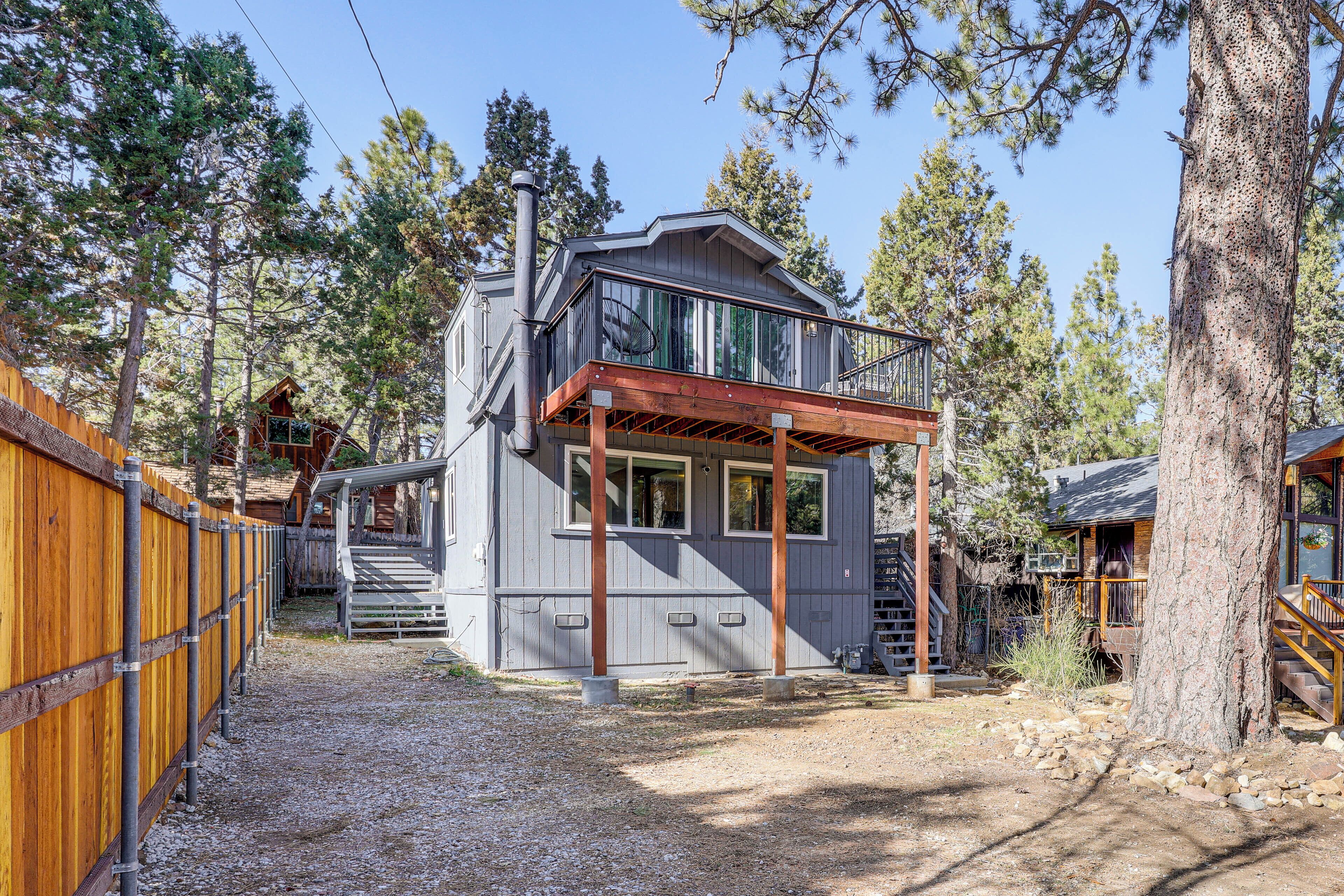 A two-story cabin with a balcony, surrounded by trees and a wooden fence.