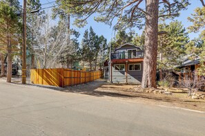 Eine zweistöckige Holzhütte mit einer Holzterrasse, umgeben von Bäumen und einem eingezäunten Garten.
