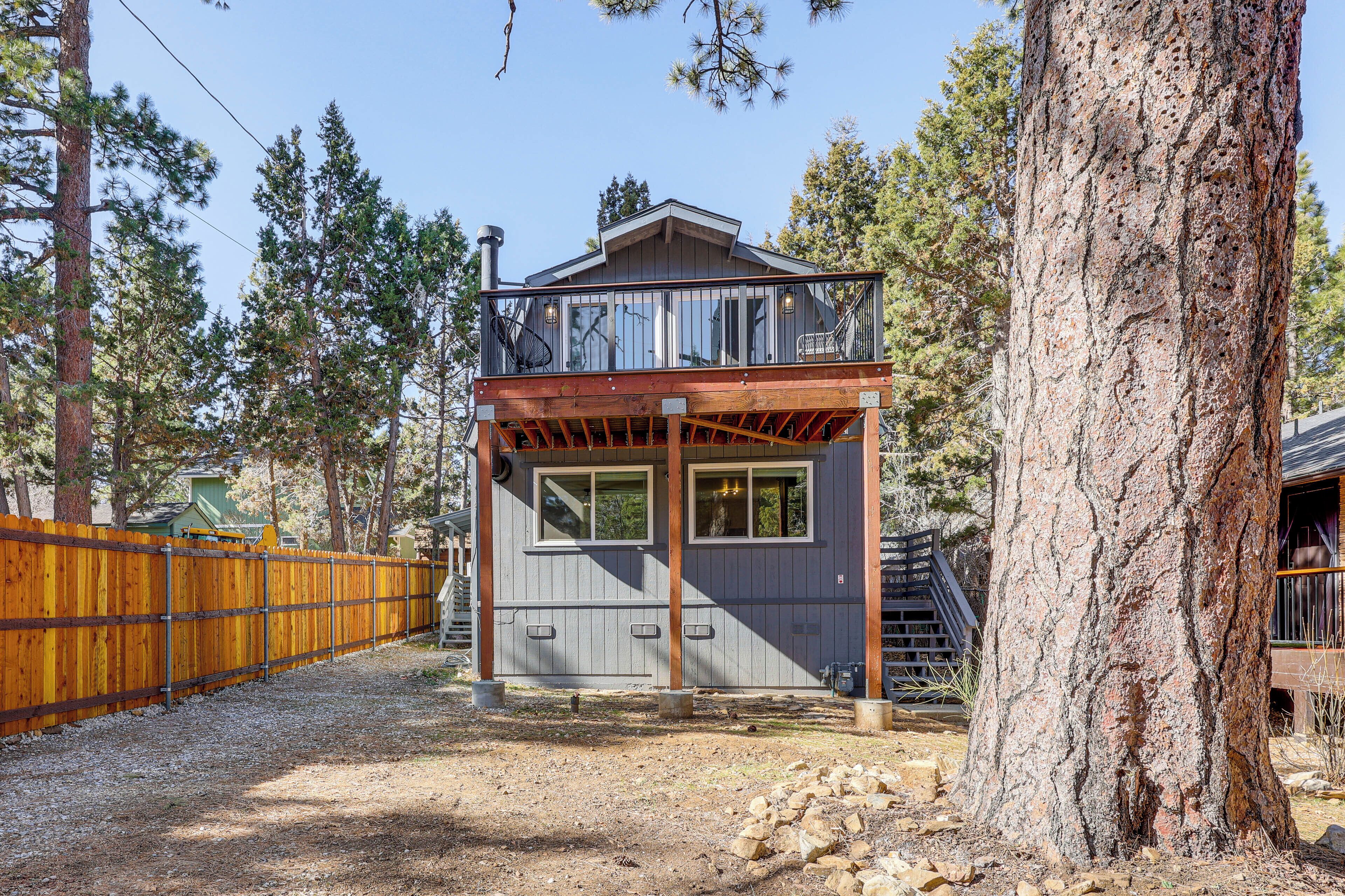 A cabin with a wooden deck, a balcony, and a large tree in the foreground.