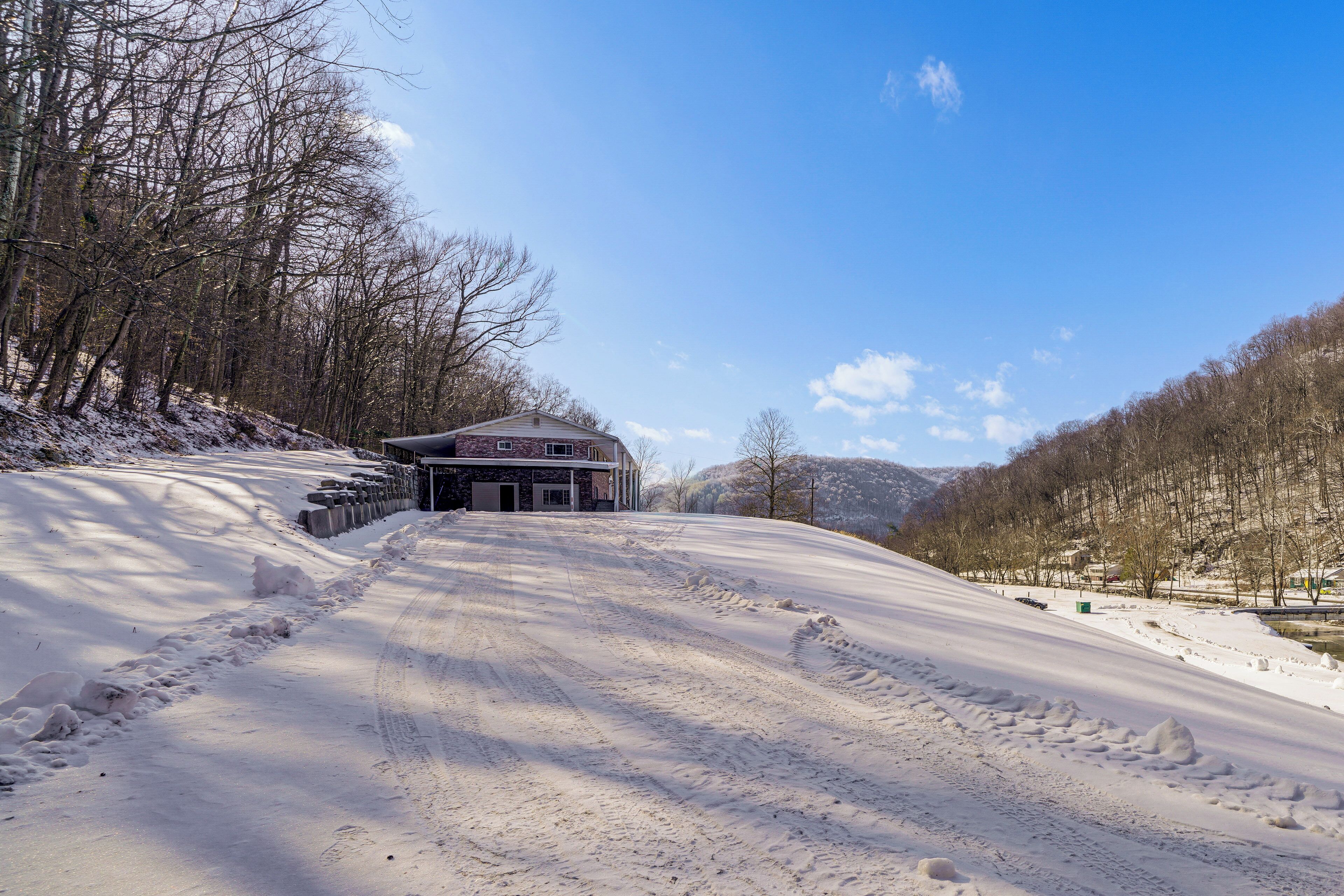 A snow-covered road leading to a building with a stone facade and a garage.