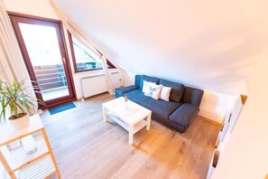 Ein kleiner, gemütlicher Wohnraum mit einem dunkelgrauen Sofa, einem weißen Couchtisch und einem Blumentopf.