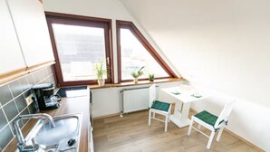 Een keuken met een raam, een radiator, een spoelbak en een kleine eettafel met stoelen.