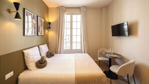 Una camera d'albergo con un letto, una scrivania con sedie, una televisione e una finestra con tende.