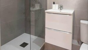 Un bagno moderno con doccia vetrata, lavabo bianco e specchio soprastante.