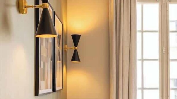 Una camera d'albergo con un letto, due cuscini, una lampada a parete e una finestra con tende.