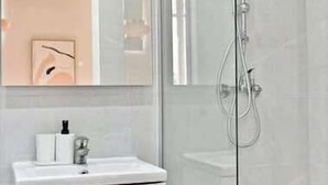 Ein modernes Badezimmer mit Duschkabine aus Glas, einem weißen Waschbecken und einem Spiegel darüber.
