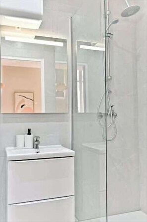Ein modernes Badezimmer mit Duschkabine aus Glas, einem weißen Waschbecken und einem Spiegel darüber.