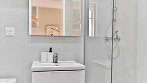 Ein modernes Badezimmer mit Duschkabine aus Glas, einem weißen Waschbecken mit Spiegel darüber und einer Toilette links.
