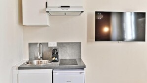 Eine kompakte Küche mit integriertem Geschirrspüler, einer Edelstahl-Spüle, einer Kaffeemaschine und einem flachbildschirmigen Fernseher an der Wand.