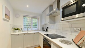 Una cucina moderna con mobili bianchi, un forno a microonde nero, un forno integrato e una finestra con persiane.