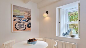 Un'area pranzo con un tavolo rotondo, sedie bianche, una ciotola piena di pigne e un quadro appeso al muro.